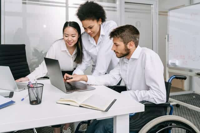 Grupo de advogados conversam olhando para o computador. Todos usam roupas sociais e parecem estar num escritório.