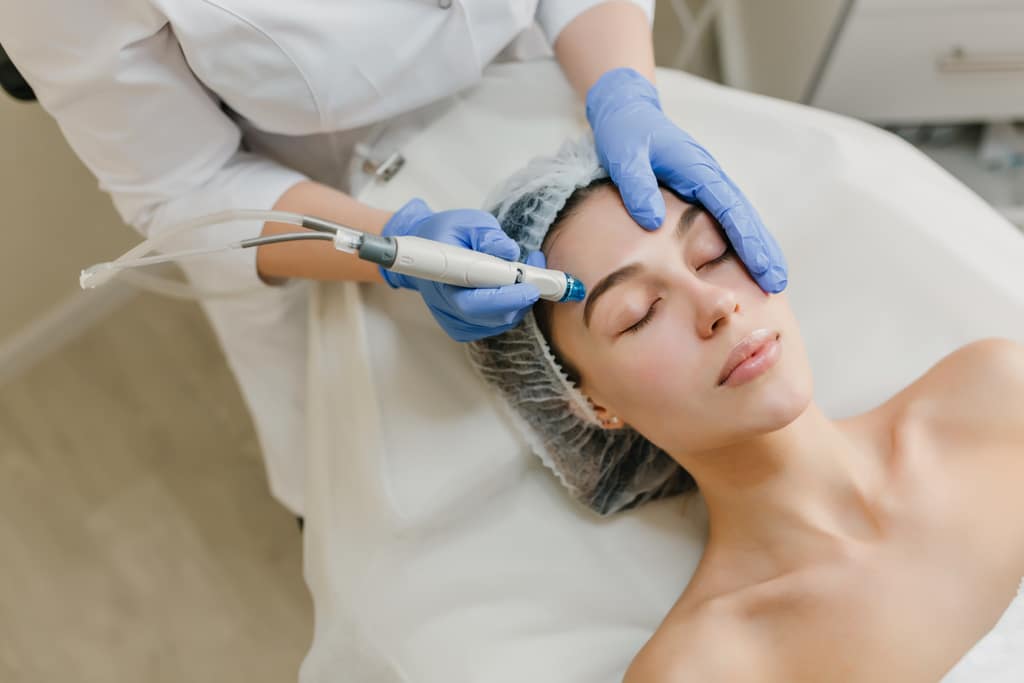 Profissional realiza procedimento estético facial em paciente utilizando equipamento especializado e luvas de proteção.