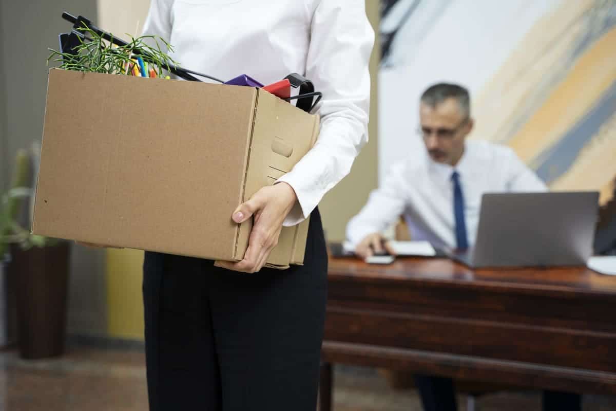 Profissional segurando caixa com objetos pessoais ao sair do trabalho após demissão sem justa causa.